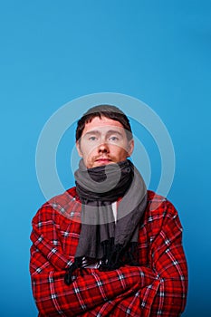 A wrapped in a blanket sick man with scarf is standingon blu background.