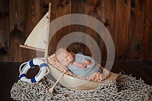 Wrapped in blue fabric, a newborn sleeping baby lies in a wooden sailing boat