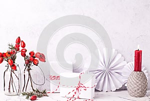 Wrapped boxes with presents, briar berries in bottle, paper, rosettes, burning red candle against textured  wall.