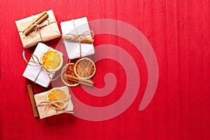 Wrapped boxes with presents decorated cinnamon,  slices dried oranges on  red textured  paper background.