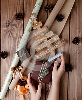 Wrapped Christmas gifts in craft paper on wooden table. Process of wrapping gifts. Lifestyle background. View from above.