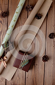 Wrapped Christmas gifts in craft paper on wooden table. Process of wrapping gifts. Lifestyle background. View from above.