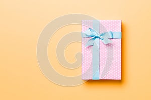 Wrapped Christmas or other holiday handmade present in paper with blue ribbon on orange background. Present box, decoration of
