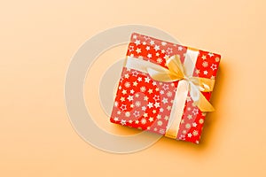 Wrapped Christmas or other holiday handmade present in paper with Gold ribbon on orange background. Present box, decoration of