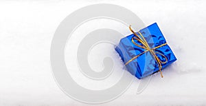 Wrapped classic blue gift box with gold ribbon lies in the white snow. Celebration background. Winter birthday, party, fun, joy