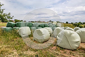 Wrapped hay bales in green and white foil stacked on dry yellowish-green grass on German farmland