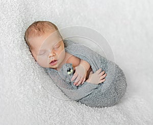 Wrapped sleeping baby with opened mouth holding little toy