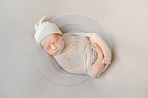 Wrapped sleeping newborn baby in white hat