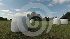 Wrapped white hay bales on farmland, time lapse