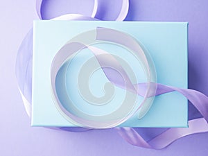 Wrapping blue pastel present box with ribbon on purple background