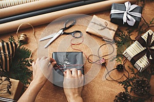 Wrapping christmas gifts flat lay. Hands wrapping stylish christmas gift box in black paper and scissors, rustic presents, thread