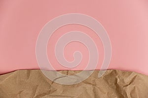Wrapping paper against a pink background. Crumpled sheet of light brown paper lies on colored surface. Top view. Copy space for