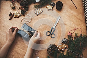 Wrapping rustic christmas gift. Hands wrapping christmas gift in stylish black paper and pine branches, cones, gingerbread cookies