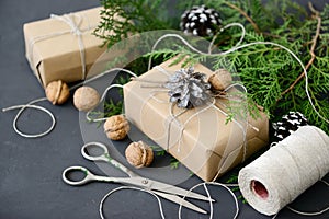 Wrapping rustic eco Christmas gifts with craft paper, string and natural fir branches on dark background