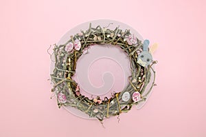 Wreath of branches on pink background with colorful easter egg candies, flowers and bunny figures. Easter concept
