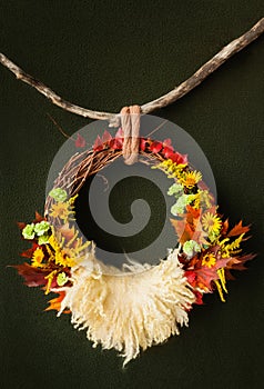 A wreath of vines in autumn yellow leaves hangs on a branch on an dark green background for a photo shoot