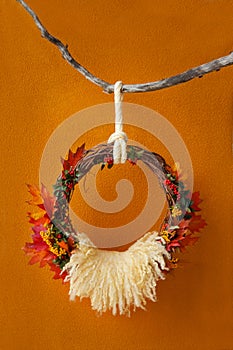 A wreath of vines in autumn yellow leaves hangs on a branch on an orange background