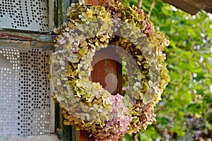 Wreath of withering hydrangeas on the window of an old house .
