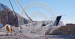 Wreckage of abandoned sunken yacht sailing boat washed ashore lie near a rock