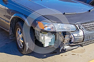 Wrecked car - silver blue sedan showing passenger front that has been in accident with part of bumper missing so you can see