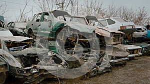 Wrecked vehicles are placed on top of one another on junkyard.