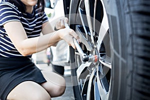 Wrench in hands of woman,flat car tire,trying to change wheel after a car breakdown,difficulty in emergency repair,accident with