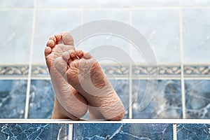 Wrinkled bare feet coming out from a bathtub. Young person getting a bath feet close-up indoor in bathroom interrior photo photo