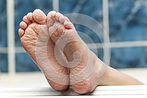 Wrinkled bare feet coming out from a bathtub. Young person getting a bath feet close-up indoor in bathroom interrior photo