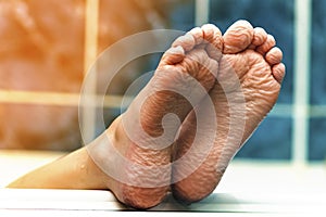 Wrinkled bare feet coming out from a bathtub. Young person getting a bath feet close-up indoor in bathroom interrior photo