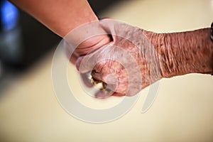 Wrinkled elderly woman`s hand holding to young man`s hand, walking in shopping mall. Family Relation, Health, Help, Support concep