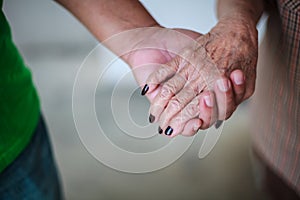 Wrinkled elderly woman`s hand holding to young man`s hand, walking in shopping mall park. Family Relation, Health, Help, Support