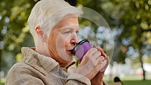 Wrinkled face of 60s happy elderly woman outdoors in park looking aside having wide smile, dental implants and