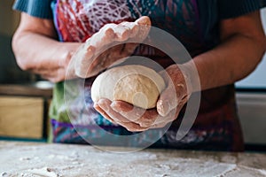 Wrinkled grandmothers hands holding and kneading fresh bread dough photo
