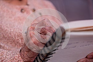 wrinkled hands for elderly person writing notes on here note book in living room