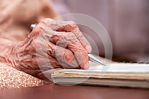 wrinkled hands for elderly person writing notes on his note book in living room