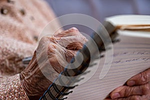 wrinkled hands for elderly person writing notes on here note book in living room