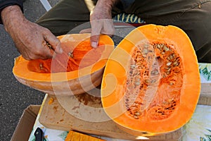 Wrinkled hands scooping out a ripe pumpkin from the seeds