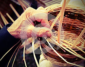 wrinkled hands of the senior craftsman while creating a wicker b