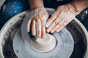 Wrinkled hands wizard on potter wheel makes clay dishes. Place to work