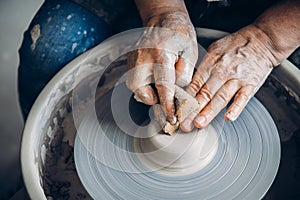 Wrinkled hands wizard on potter wheel makes clay dishes. Place to work. Top view