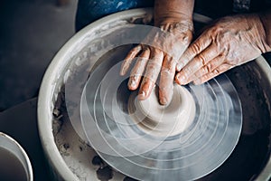 Wrinkled hands wizard on potter wheel makes clay dishes. Place to work. Top view