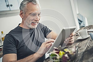 Wrinkled handsome man reading recipes on his tablet