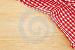 Wrinkled red gingham fabric on rustic light brown wood background.