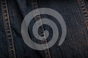 Wrinkled worn denim or grunge jeans fabric texture with orange tint and seams. Close up background or backdrop. Textile