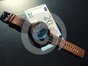 Wrist watch with leather strap near the banknote on a dark background