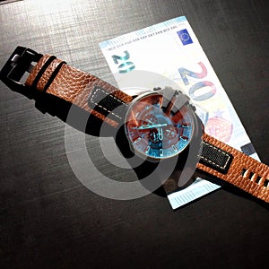 Wrist watch with leather strap near the banknote on a dark background