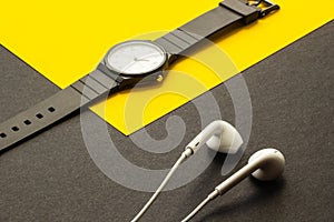 Wrist watch and white headphones on black and yellow background