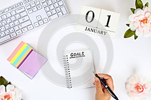 Write a goal for the new year 2010 in a white notebook on a white desktop next to a coffee mug and a keyboard. Top view, flat layo