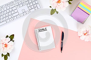 Write a goal for the new year 2010 in a white notebook on a white desktop next to a coffee mug and a keyboard. Top view, flat layo