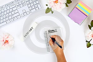 Write a goal for the new year 2010 in a white notebook on a white desktop next to a coffee mug and a keyboard. Top view, flat layo